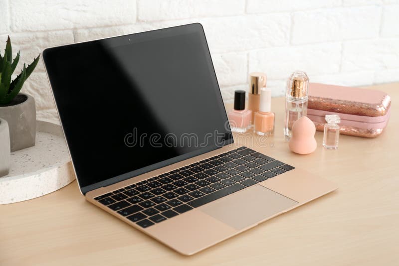 Posto di lavoro alla moda con il computer portatile moderno e prodotti cosmetici sulla tavola vicino al muro di mattoni immagine stock Posto di lavoro alla moda con il computer portatile moderno e prodotti cosmetici sulla tavola vicino al muro di mattoni immagine stock