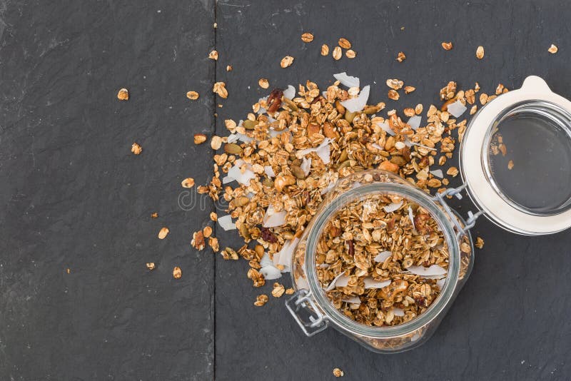Pot en verre de granola organique faite maison avec la noix de coco et les noix de pécan sur le fond noir C?r?ale de petit d?jeun images stock Pot en verre de granola organique faite maison avec la noix de coco et les noix de pécan sur le fond noir C?r?ale de petit d?jeun images stock