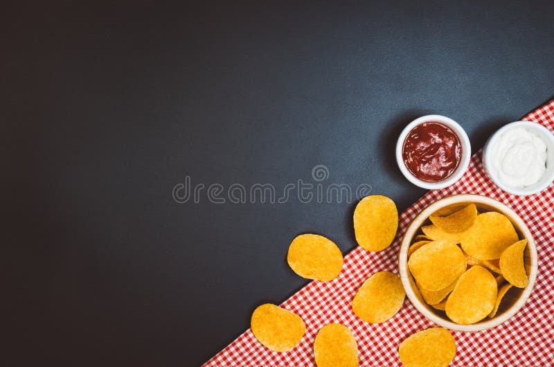 Potatischiper och mellanmål på svart kritiserar tabellen, bästa sikt royaltyfri fotografi Potatischiper och mellanmål på svart kritiserar tabellen, bästa sikt royaltyfri fotografi