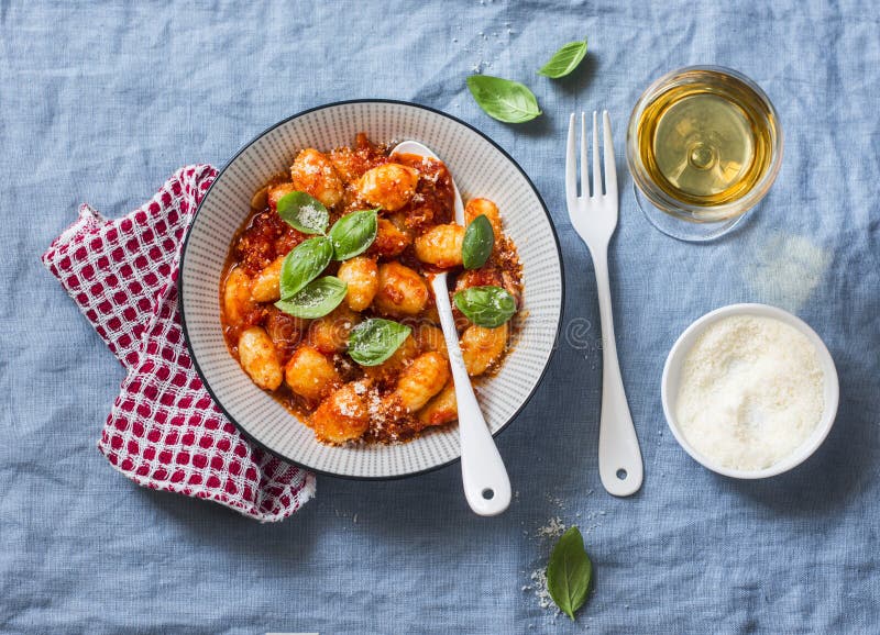 Potato gnocchi in tomato sauce with basil and parmesan and a glass of white wine on blue background, top view. Italian cuisine.