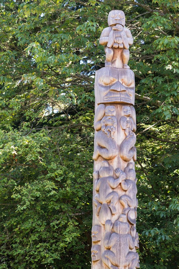 Vancouver, Canada - July 24, 2016: One of nine totem poles at Hallelujah point in Stanley Park. Plain wooden with images of man holding eagle, eagle holding baby, frog, masks. Green trees as background. Vancouver, Canada - July 24, 2016: One of nine totem poles at Hallelujah point in Stanley Park. Plain wooden with images of man holding eagle, eagle holding baby, frog, masks. Green trees as background.