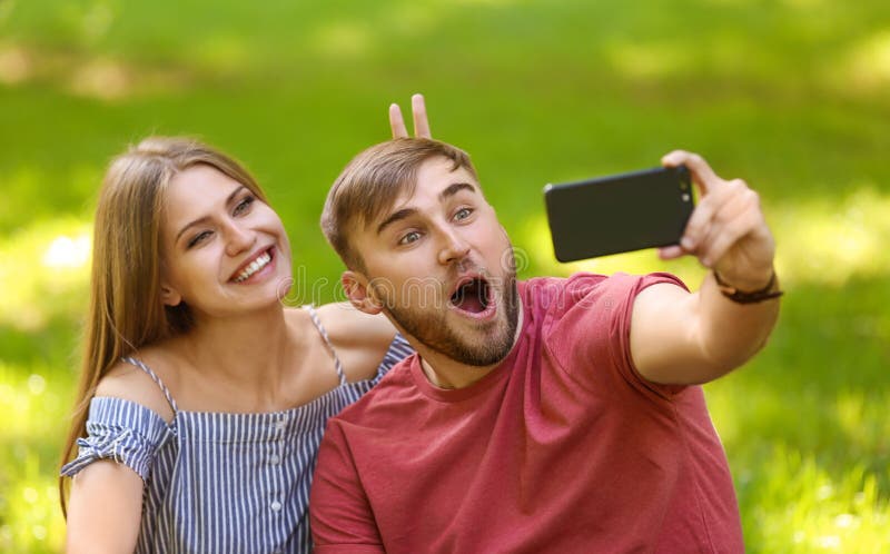 Potomstwa dobierają się brać selfie na zielonej trawie w parku zdjęcia royalty free Potomstwa dobierają się brać selfie na zielonej trawie w parku zdjęcia royalty free