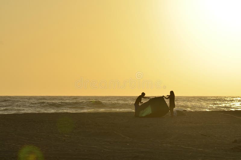 Potomstwa dobierają się mężczyzna i kobiety sylwetki stawia w górę namiotu na tropikalnej plaży fotografia royalty free Potomstwa dobierają się mężczyzna i kobiety sylwetki stawia w górę namiotu na tropikalnej plaży fotografia royalty free