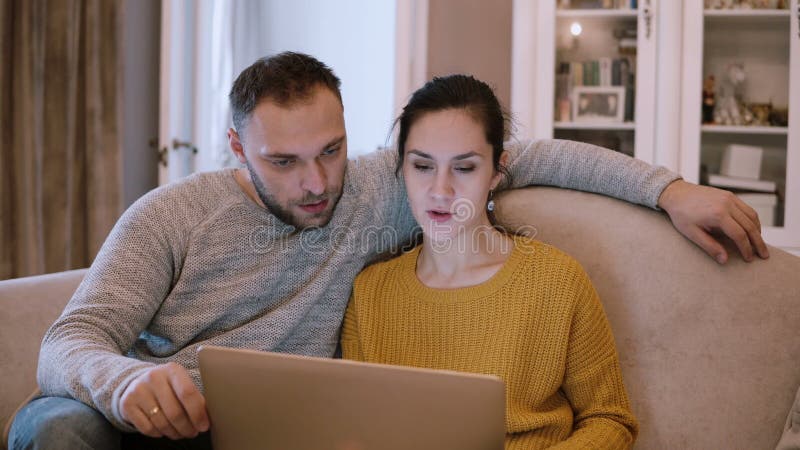 Potomstwa dobierają się obsiadanie na leżanki i mienia komputerze Mężczyzna i kobieta używa laptop przy żywym pokojem podczas gdy