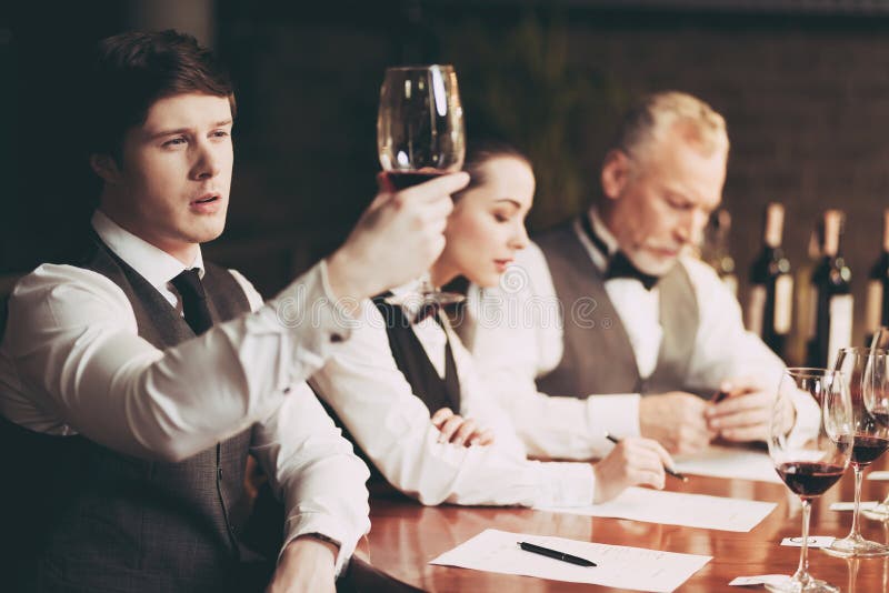 Potomstwa doświadczali sommelier spojrzenia przy cedziny wino w szkle czara ręki degustaci wino zdjęcia stock Potomstwa doświadczali sommelier spojrzenia przy cedziny wino w szkle czara ręki degustaci wino zdjęcia stock
