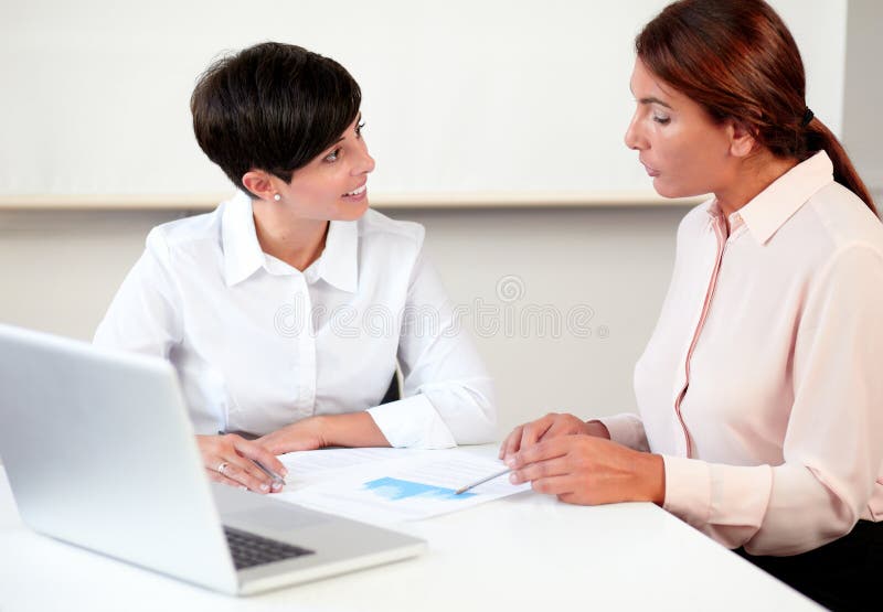 Portrait of young and mature women working on documents while sitting on office desk. Portrait of young and mature women working on documents while sitting on office desk