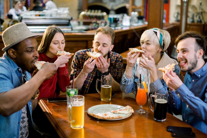 Potomstwa pięć ludzi je pizzę i śmia się podczas gdy siedzący w fast food restauracji Grupa przyjaciele cieszy się podczas gdy obrazy stock Potomstwa pięć ludzi je pizzę i śmia się podczas gdy siedzący w fast food restauracji Grupa przyjaciele cieszy się podczas gdy obrazy stock