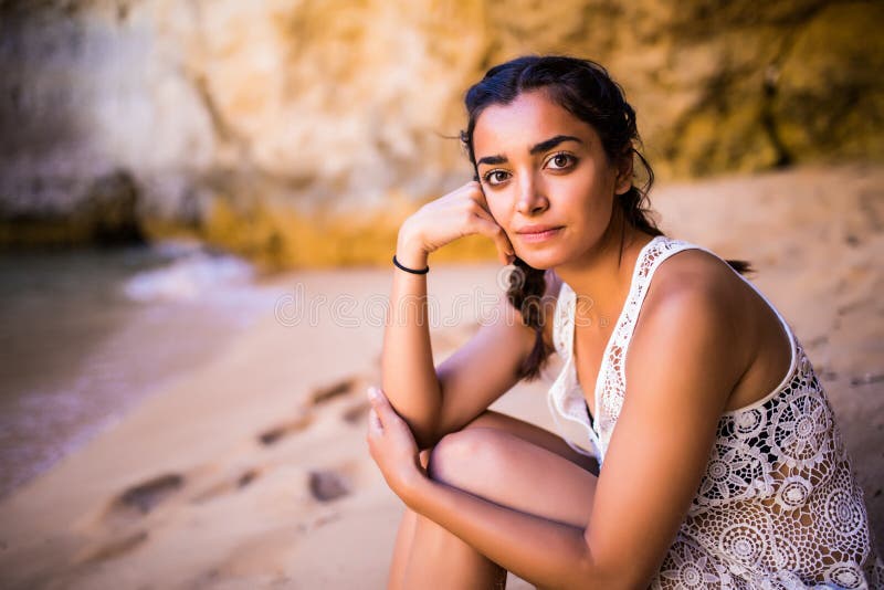 Potrait maxican girl sitting on golden sand at beach near rocks and looking at ocean. Summer vocation