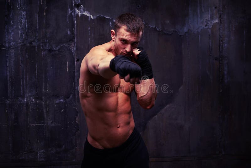 Potężny sportowiec ćwiczy dźgnięcie w czarnych bokserskich rękawiczkach