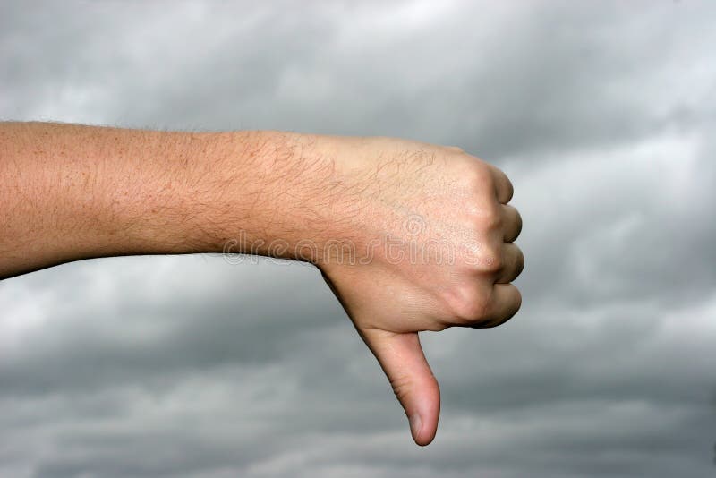 Thumb down with gray storm sky in the background. Thumb down with gray storm sky in the background