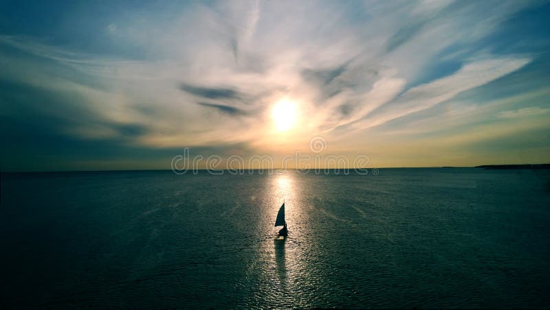Pouco barco branco que flutua na água para o horizonte nos raios do sol de ajuste Nuvens bonitas com destaque amarelo