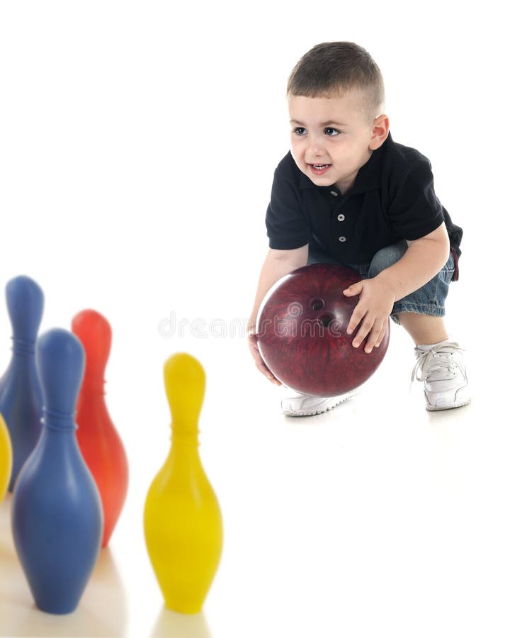 An adorable preschooler attempting to bowl a heavy bowling ball to knock down his toy plastic pins. Focus on child. On a white background. An adorable preschooler attempting to bowl a heavy bowling ball to knock down his toy plastic pins. Focus on child. On a white background.