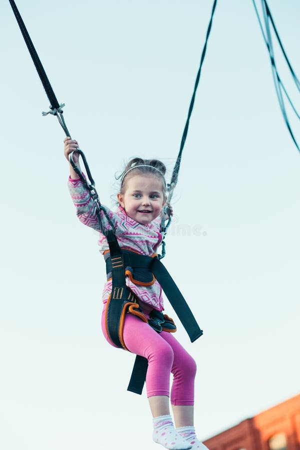 Pouco menina de sorriso adorável que salta no trampolim, tendo o divertimento no funfair imagem de stock royalty free Pouco menina de sorriso adorável que salta no trampolim, tendo o divertimento no funfair imagem de stock royalty free