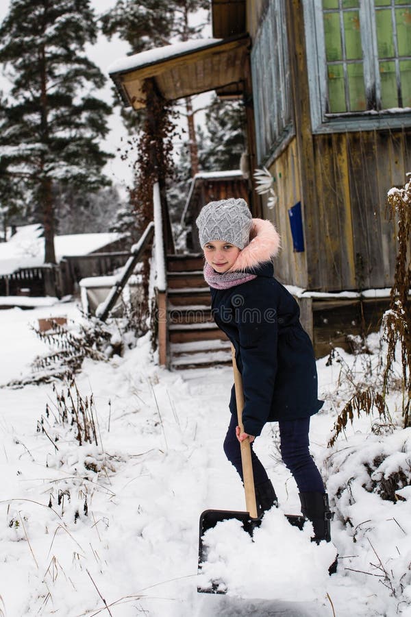 Pouco menina feliz limpa a neve perto de sua casa rural fotografia de stock Pouco menina feliz limpa a neve perto de sua casa rural fotografia de stock