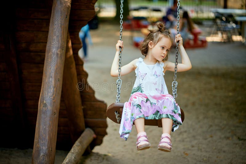 Pouco menina triste bonita no balanço com a cara pensativa no campo de jogos imagens de stock Pouco menina triste bonita no balanço com a cara pensativa no campo de jogos imagens de stock
