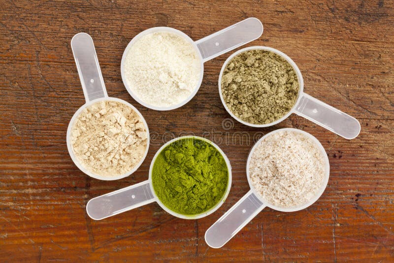 Five plastic measuring cups of different superfood supplement powders (form bottom clockwise: wheatgrass, maca root, whey protein, hemp seed protein, psyllium husk) on grunge wood background. Five plastic measuring cups of different superfood supplement powders (form bottom clockwise: wheatgrass, maca root, whey protein, hemp seed protein, psyllium husk) on grunge wood background