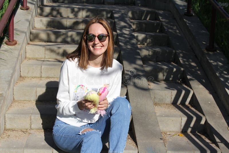 Dolls in the hands of an unrecognizable young girl sitting on the steps. Knitted handmade dolls. Knitting. Hobby. 2 dolls with long hair in the hands of a young girl in nature. Fashion. Dolls in the hands of an unrecognizable young girl sitting on the steps. Knitted handmade dolls. Knitting. Hobby. 2 dolls with long hair in the hands of a young girl in nature. Fashion.