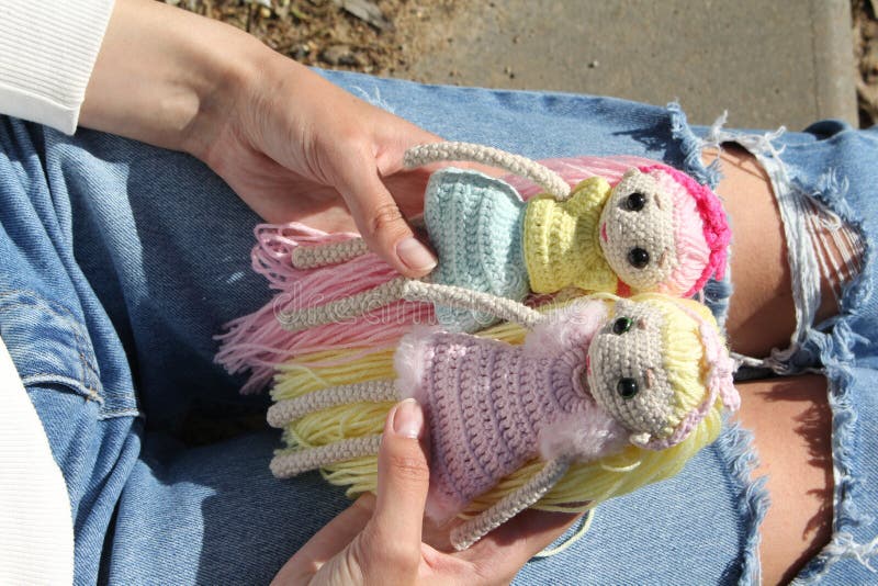 Dolls in the hands of an unrecognizable young girl sitting on the steps. Knitted handmade dolls. Knitting. Hobby. 2 dolls with long hair in the hands of a young girl in nature. Fashion. Dolls in the hands of an unrecognizable young girl sitting on the steps. Knitted handmade dolls. Knitting. Hobby. 2 dolls with long hair in the hands of a young girl in nature. Fashion.