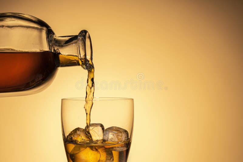 Pouring an alcoholic beverage from a bottle into a glass. Whiskey, Bourbon, or liqueur on the rocks. Bright juicy photo, close-up