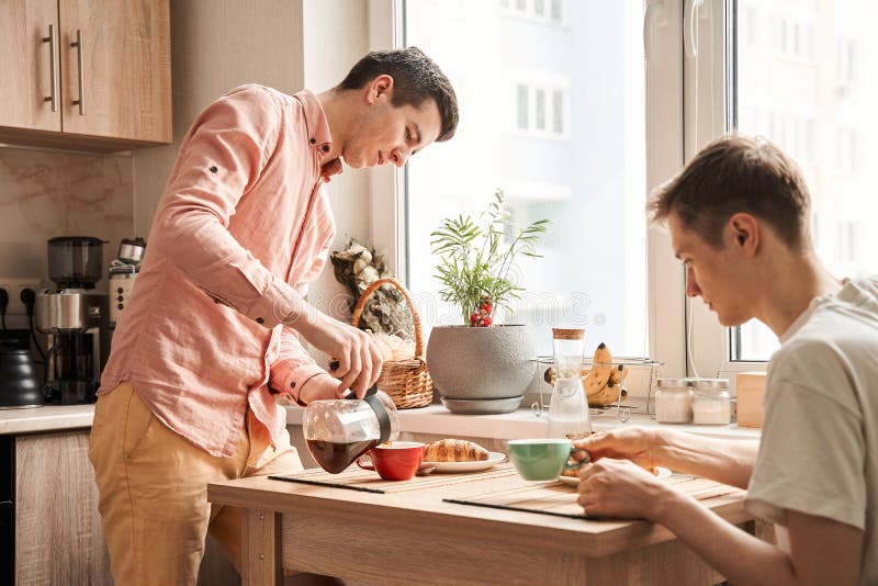 Gay wearing shirt pouring coffee to cup for breakfast for him and his boyfriend
