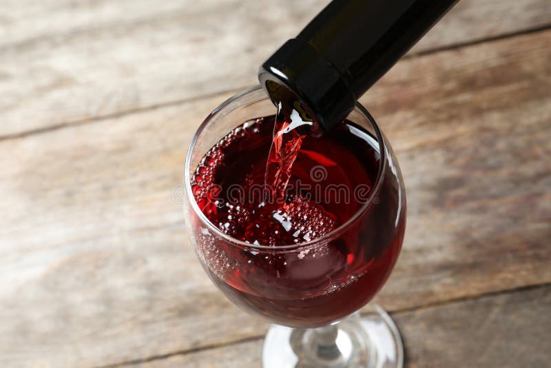 Versare un bicchiere di vino in vetro su sfondo di legno.