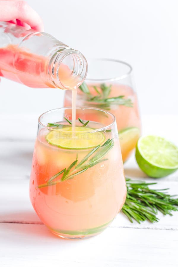 Pouring Fresh Juice in Glass with Lime and Rosemary on White Background