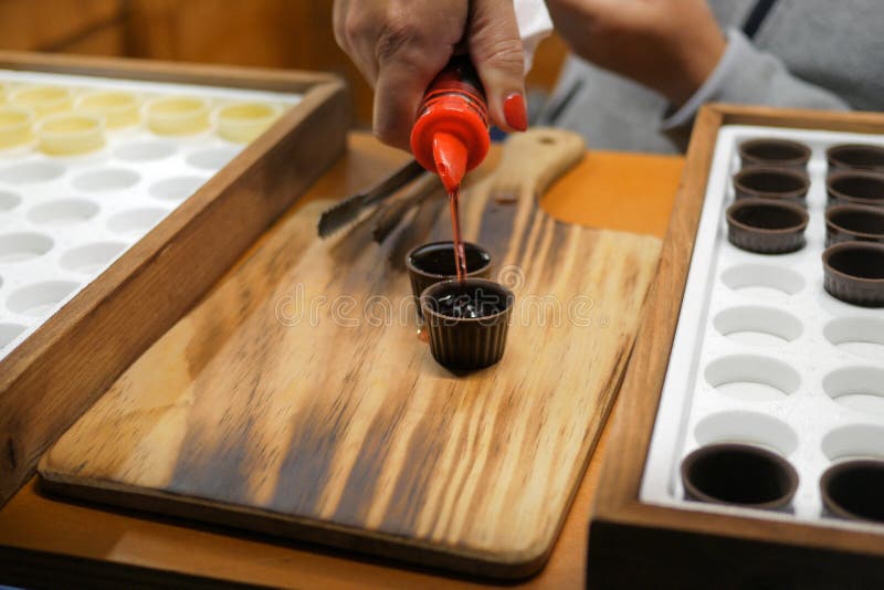 Pouring Ginja / Ginjinha cherry liqueur drink into chocolate cups on Wooden background. Traditional Portuguese drink