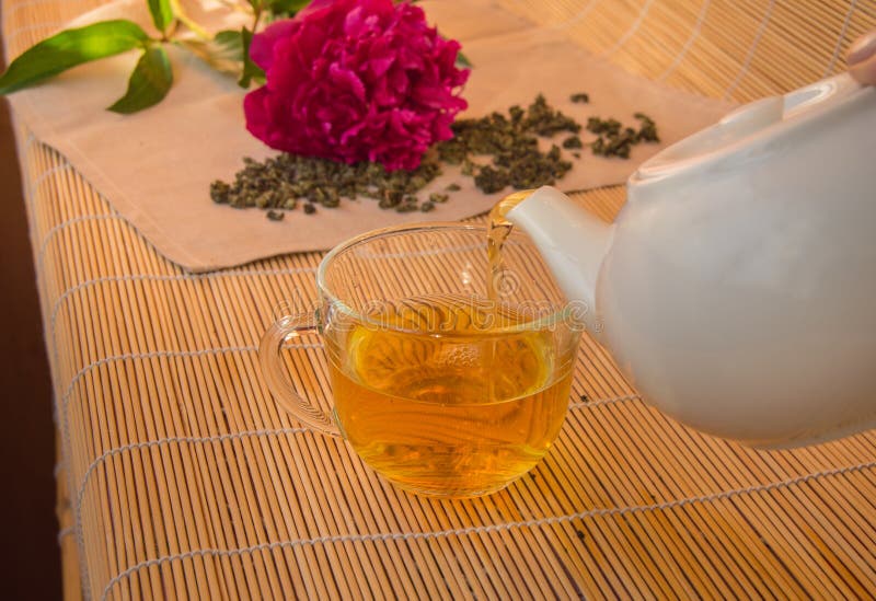 Pouring Green Tea from a White Ceramic Teapot in Glass Cup Stock Photo