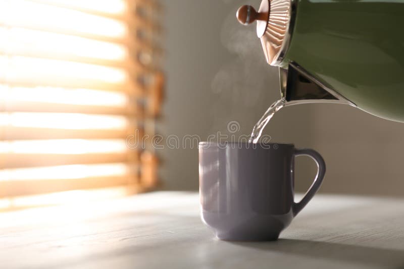 Pouring hot water into cup on white wooden table, space for text. Good morning