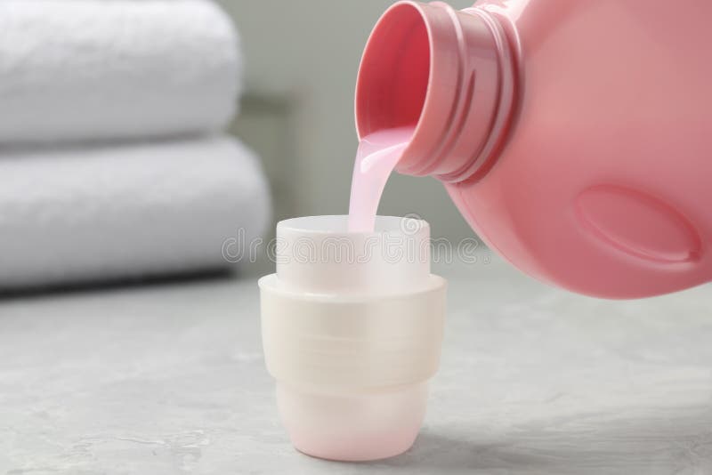 Pouring Laundry Detergent from Bottle into Cap on Light Grey Marble