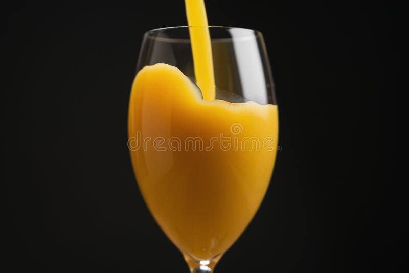 Pouring orange juice into glass over black background