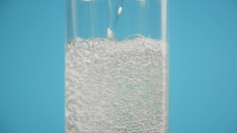 Pouring soda in glass on blue background, clean sparkling water pours slow