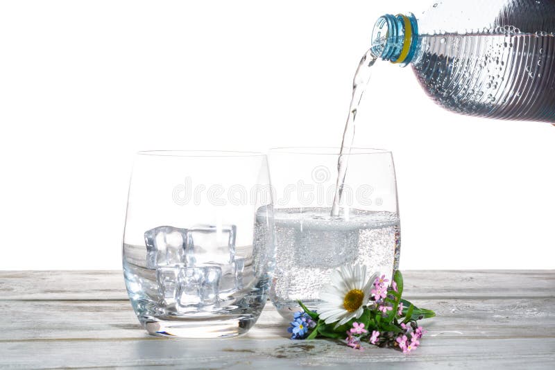 Pouring of sparkling soda mineral drink water in glasses with ice cubes close up copy space