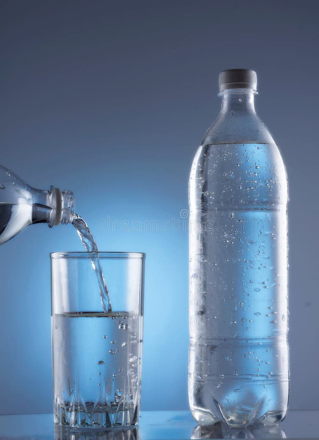 Pouring water from bottle into glass on blue background stock photos Pouring water from bottle into glass on blue background stock photos