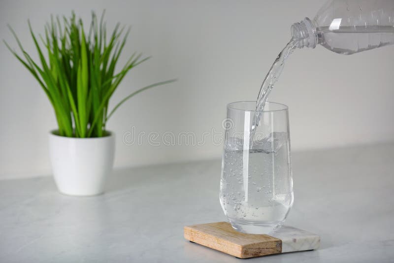 Pouring Water from Bottle into Glass on White Countertop in Kitchen