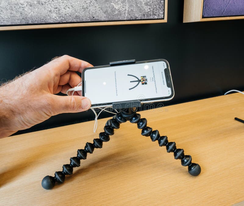 Paris, France - Mar 19 2019: POV man holding iPhone XS on the Joby Gorillapod tripod on the accessories stand inside minimalist and luxury design of Apple Store Champs-Elysees largest French store