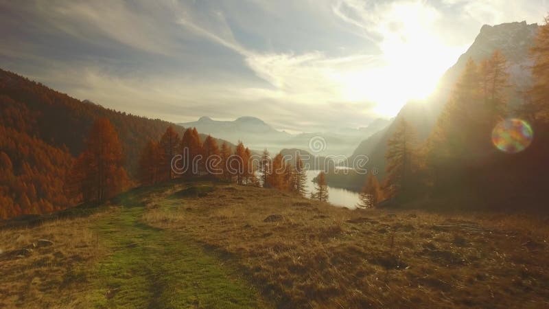 POV walking on fall path to woods,valley lake and snowy mounts at sunset with sun flare.Sunny autumn day Hiking in