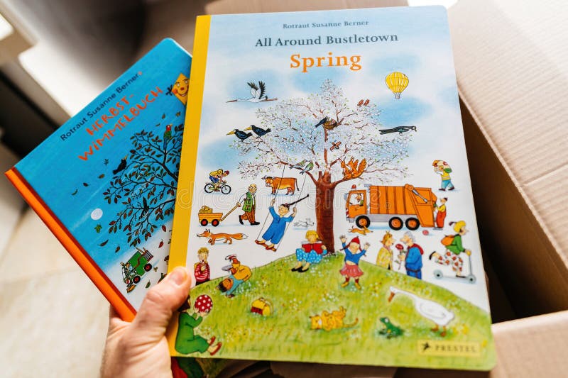 Paris, France - Mar 1, 2023: POV male hand holding Wimmelbilderbuch by Rotraut Susanne Berner - hidden picture book is a type of large-format, wordless picture book from the well-known German author. Paris, France - Mar 1, 2023: POV male hand holding Wimmelbilderbuch by Rotraut Susanne Berner - hidden picture book is a type of large-format, wordless picture book from the well-known German author