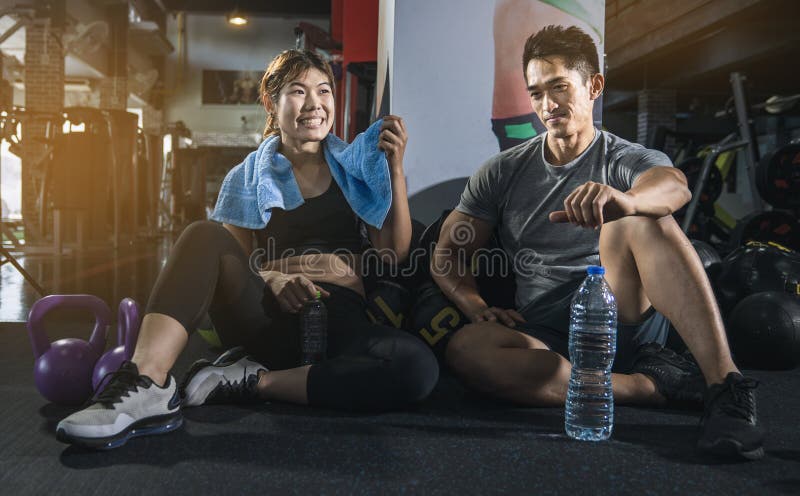 Povos aptos na engrenagem do exercício que senta-se junto no assoalho de um gym que riem junto após um exercício fotografia de stock royalty free Povos aptos na engrenagem do exercício que senta-se junto no assoalho de um gym que riem junto após um exercício fotografia de stock royalty free