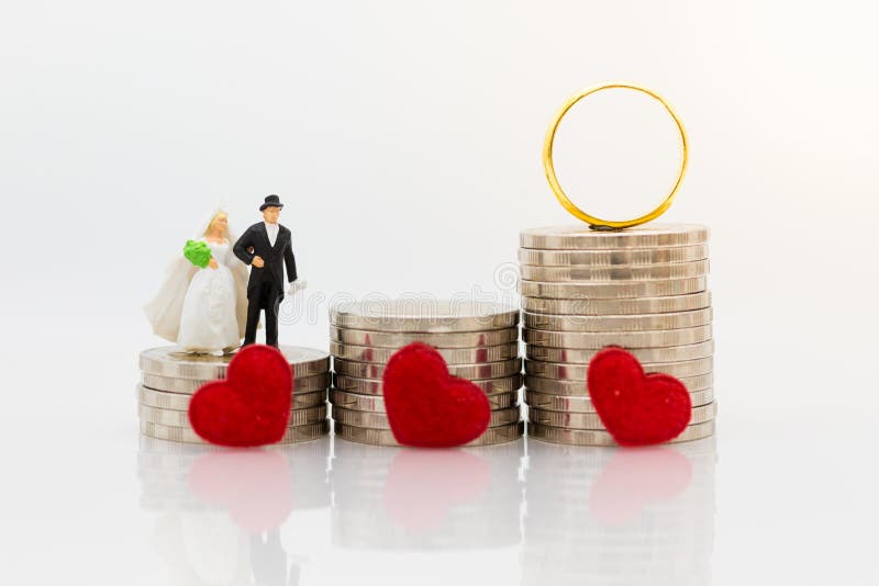 Povos diminutos: Noivos que estão na pilha de moedas com alianças de casamento O uso da imagem para salvar o dinheiro para casa-s fotografia de stock Povos diminutos: Noivos que estão na pilha de moedas com alianças de casamento O uso da imagem para salvar o dinheiro para casa-s fotografia de stock