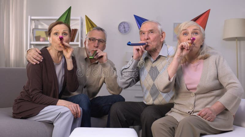 Povos envelhecidos alegres nos chapéus do aniversário que fundem no chifre do partido, celebração, partido