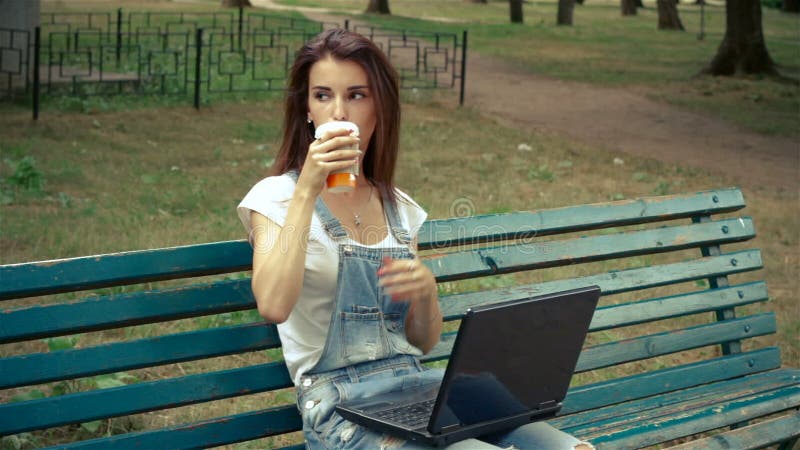 Powabna młoda brunetka siedzi w parku z laptopem