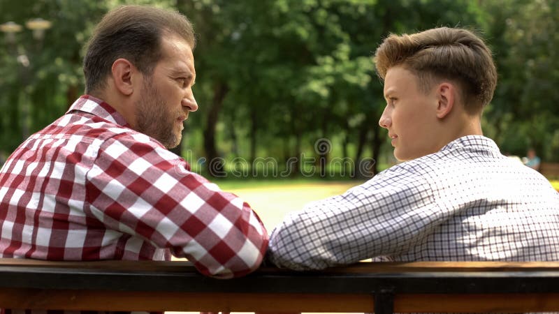 Poważny syn i tata opowiada na ławce w parku, ojca udzielenia życia doświadczenie obraz stock Poważny syn i tata opowiada na ławce w parku, ojca udzielenia życia doświadczenie obraz stock