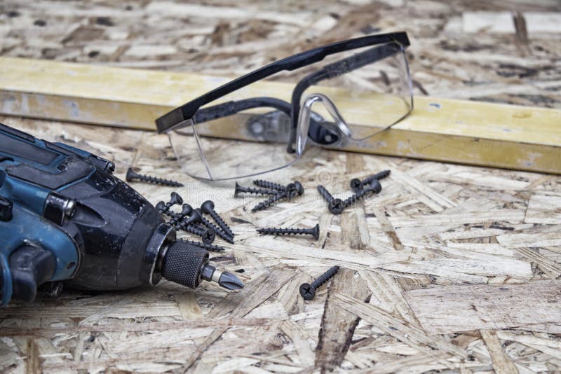 Power drill with goggles for eye safety and building level against the background of OSB panel. Concept on the topic of. Construction and repair royalty free stock photo Power drill with goggles for eye safety and building level against the background of OSB panel. Concept on the topic of. Construction and repair royalty free stock photo