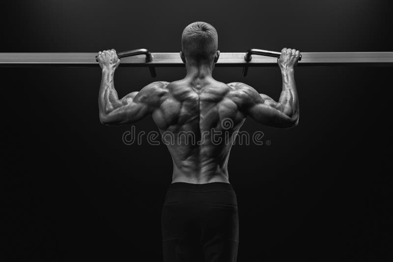 Black and white image of power muscular bodybuilder guy doing pullups in gym. Fitness man pumping up lats muscles. Fitness and bodybuilding training health lifestyle concept