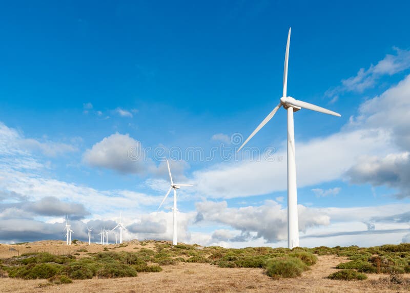 Power plant with wind turbines in open field background. Various mountain wind turbine with green grass and cloudy sky