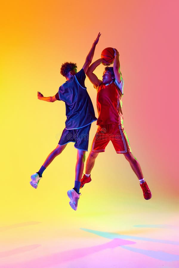 Powerful slam dunk. Dynamic basketball practice session with two athletes in neon light against gradient studio royalty free stock photos