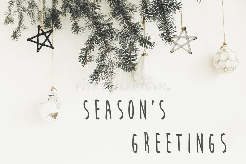 Pozdrowienia sezonu podpisać na stylowych gałęziach świątecznych ze szklanymi nowoczesnymi ozdobami wiszącymi na białym murze Świ