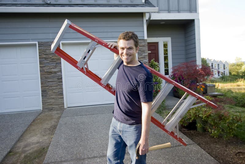 Smiling man standing in front of house holding ladder and hammer. Horizontally framed photo. Smiling man standing in front of house holding ladder and hammer. Horizontally framed photo.
