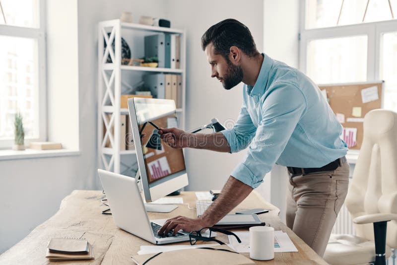 Paying attention to every detail. Young modern businessman analyzing data using computer while working in the office. Paying attention to every detail. Young modern businessman analyzing data using computer while working in the office